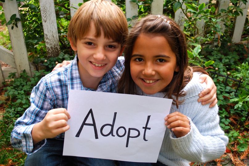 Two children holding paper with word ADOPT